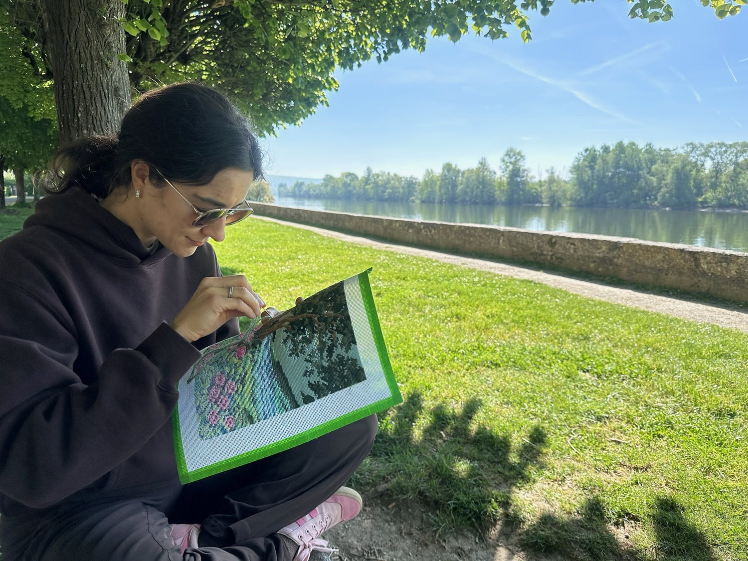 Katerina stitching a needlepoint canvas beside a river